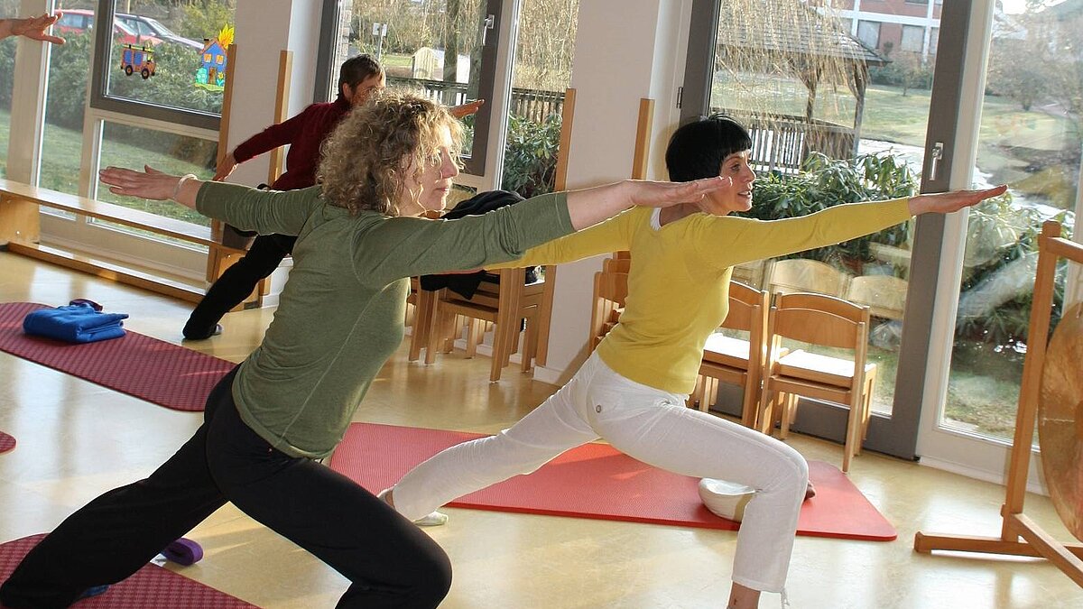 Yoga-Kurs Ein Yogakurs im Ludgerus-Werk. Zwei Frauen im Vordergrund machen mit erhobenen Armen die gleiche Figur. Im Hintergrund ist eine weitere Frau, die das gleiche macht.