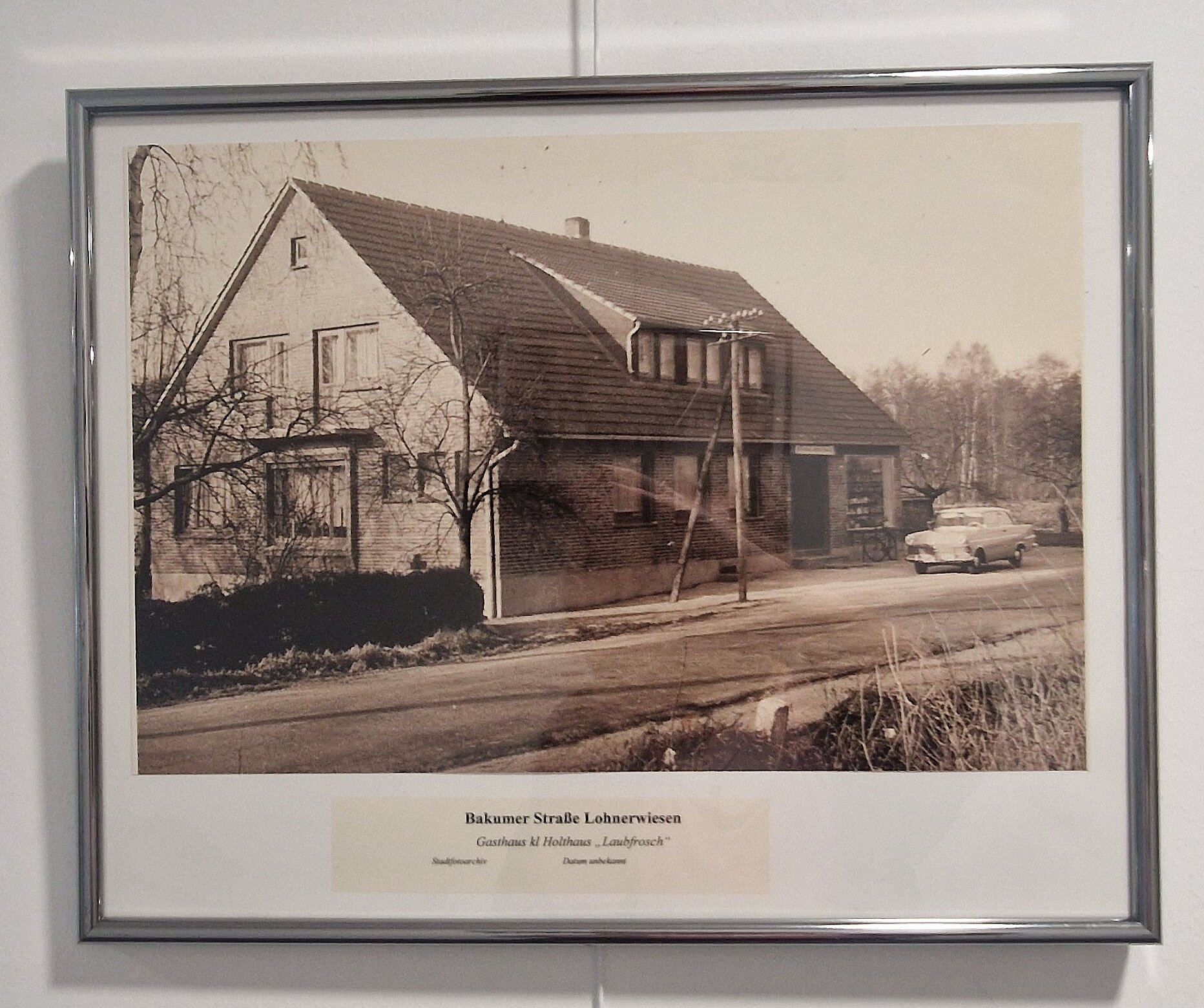 Eine schwarz-weiß Fotografie des alten Hauses das damals die Gaststätte kl. Holthaus "Laubfrosch" beherbergt hat. Vor dem Haus stehen noch ein alter Auto und ein Fahrrad. 