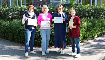 Die Organisatorinnen stehen an der Rückseite des Ludgerus-Werk zusammen. Sie halten das Schild des Bücherflohmarkts in den Händen. Es ist ein sonniger Frühlingstag. 