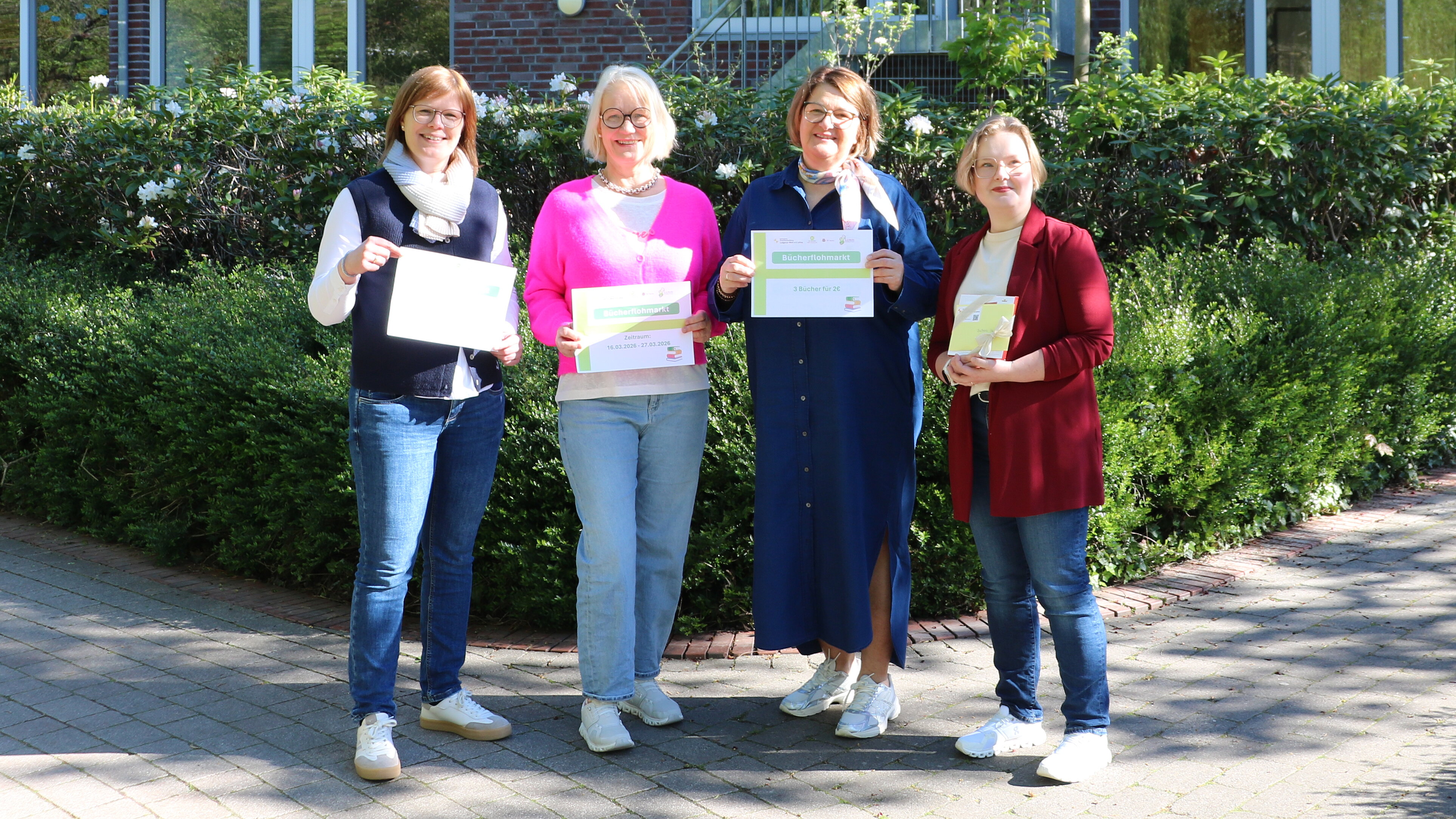 Die Organisatorinnen stehen an der Rückseite des Ludgerus-Werk zusammen. Sie halten das Schild des Bücherflohmarkts in den Händen. Es ist ein sonniger Frühlingstag.