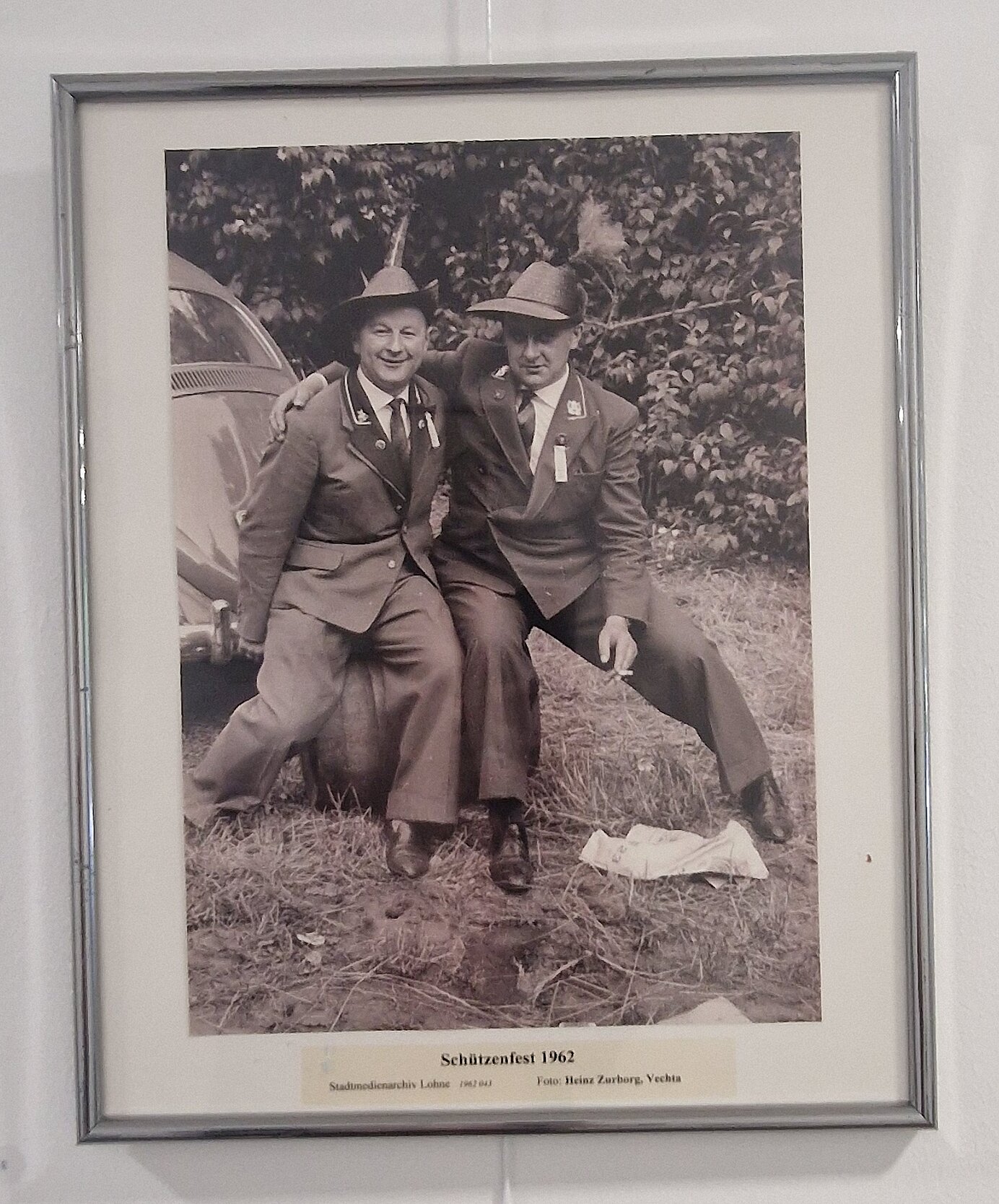 Eine schwarz-weiß Fotografie von zwei Schützen in Anzügen. Sie sitzen zusammen auf einem Fass und umarmen sich. Sie posieren für die Fotografie.