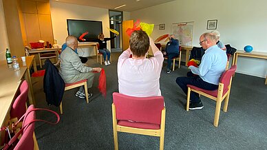 Teilnehmende sitzen mit der Dozentin in einem Stuhlkreis und machen gemeinsam Übungen. 