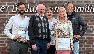 Eine Gruppe von 5 Leuten stehen vor dem Logo an der Außenwand des Ludgerus-Werk e.V. Lohne. Annette Kröger, die zweite Person von rechts, hält ein Plakat für den Vortrag "Haltung zeigen" von Marlies Stertenbrink in den Händen. 